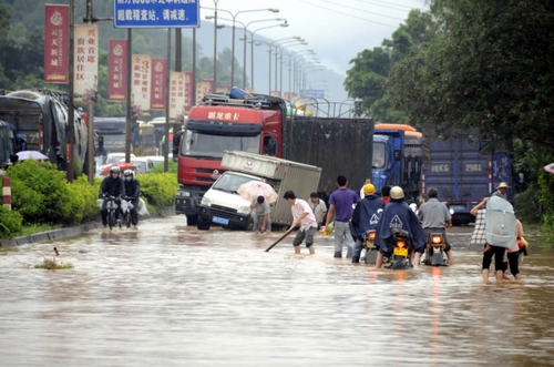 5月18日，國道324線廣西興業(yè)縣石南鎮(zhèn)黑石嶺路段被洪水淹沒，一名群眾手持木棍為摩托車探路。